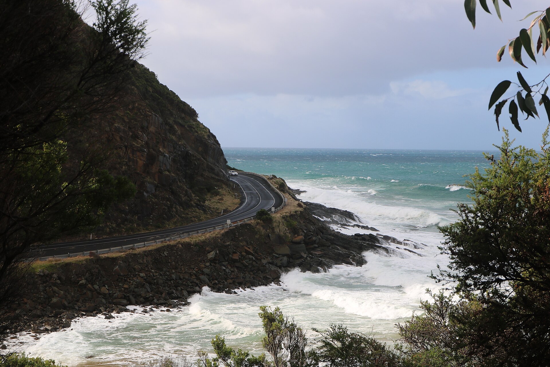 The road itself, bending along the cliff base with the surf below
